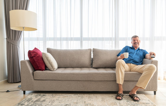 middle aged man sitting on a sofa and watching TV