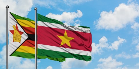 Zimbabwe and Suriname flag waving in the wind against white cloudy blue sky together. Diplomacy concept, international relations.