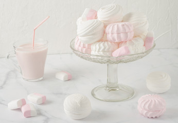 White and pink marshmallows in a glass vase on a white table. There's a glass mug of pink yogurt next to it. Soft light in high key.