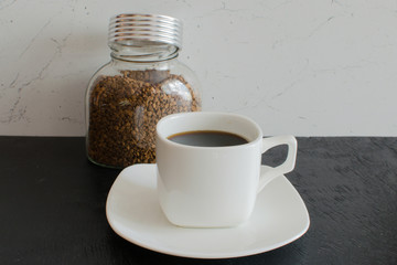 A glass jar of instant coffee in large granules next to a white mug.