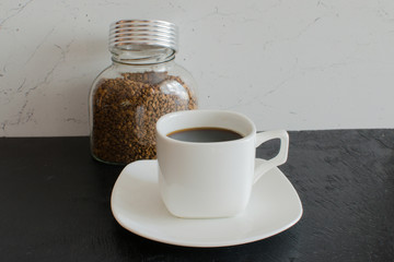 A glass jar of instant coffee in large granules next to a white mug.