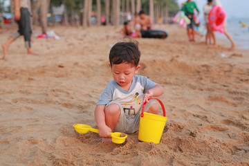 Adorable little Asian baby boy playing sand at beach.
