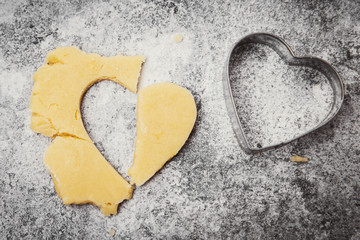 Cookie dough and metallic heart shape cutter on grey background