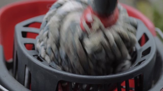 Wringing cleaning mop into red bucket close up