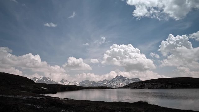 Timelapse of apline peaks with lake and cloudy sky