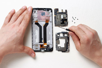Men's hands hold a screwdriver in their hands and repair a broken smartphone