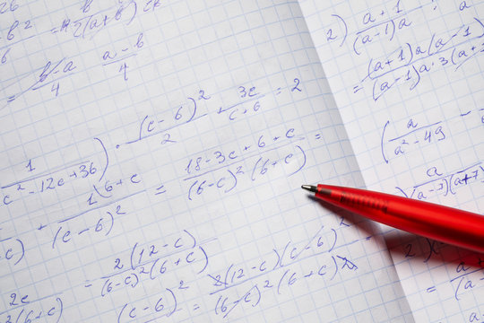 Algebraic calculations in open graph notebook with red pen. White graph paper with math fractions