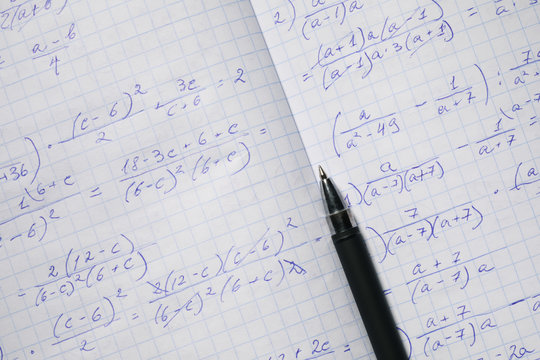 Algebraic calculations in open graph notebook with black pen. White graph paper with math fractions, top view