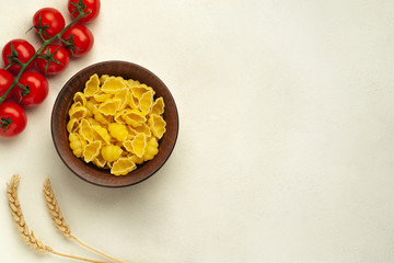 Raw pasta of hard varieties in a bowl with spikelets of wheat and cherry tomatoes on a light background with place for text top view