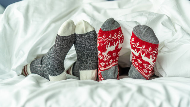Christmas socks of family couple feet relaxing on bed having good sleep time together, enjoying resting at home in bedroom for winter holiday Xmas and New Year celebration