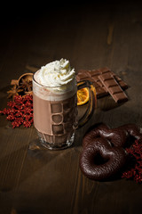 Heiße, dunkle Trinkschokolade zu Weihnachten mit Sahne, Lebkuchen, Schokoladentafel, Gewürzen, Glitzer Schneeflocken rot auf dunkel Holz Hintergrund 
