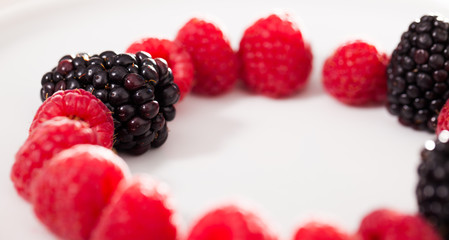 raspberries and blackberries laid out on a white plate in circle
