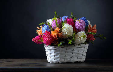 Bouquet of hyacinths in a white basket, dark background.