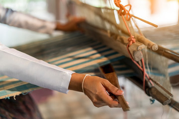 Close up hand of woman weaving silk sari on loom.female works on cotton or silk weaving with traditional hand weaving loom.Asian traditional culture. life,people, Small business,Southeast Asia concept