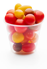 Colorful cherry tomatoes (red, garnet and yellow), fresh and raw. In plastic jar. Isolated on white background