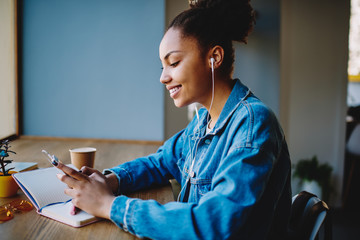 Happy cheerful female blogger searching music for creating video using application for posting...