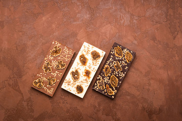 Chocolate whole tiles of various types of milky white dark on a brown background. Flat layout top view. Copy space.