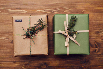 Close-up of two Christmas presents wrapped in wrapping papers decorated with fir branches on the wooden table