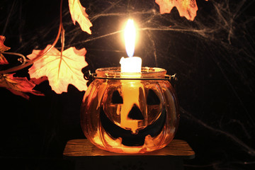 Transparent orange candlestick Halloween pumpkin with a burning candle on a black background with...