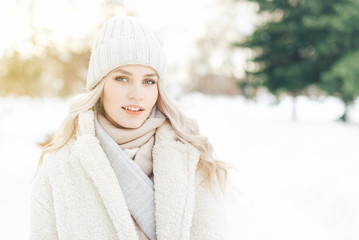 Young blonde woman winter portrait. Beautiful model girl dressed in light warm clothes looking at the camera.