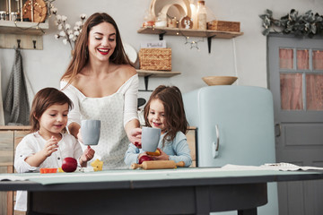 Girls is smiling. Young beautiful woman give the kids drinks while they sitting near the table with...