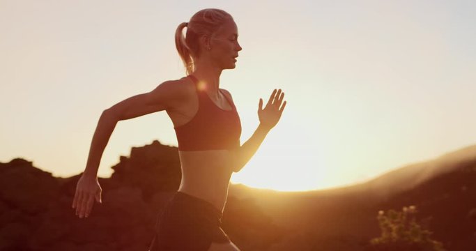 Fit attractive woman running into the golden sunset, amazing sunset workout in the mountains, determined runner training at sunset achieving her fitness goals