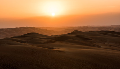 sunset in the desert, on the horizon you can see the orange sun setting behind the dunes far away