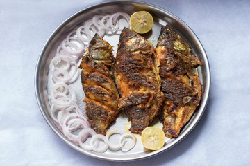 Fried mackerel fish in thali with sliced onions and lime, a Maharashtrian style food