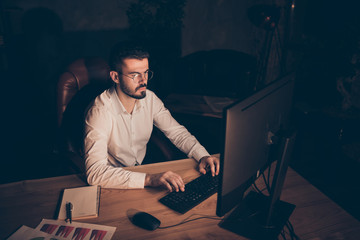 Photo of interested focused concentrated man sitting at desktop trying to make report needed to be...