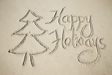 Eco-friendly Happy Holidays message handwritten in smooth sand with simple Christmas tree decorated with starfish on the beach