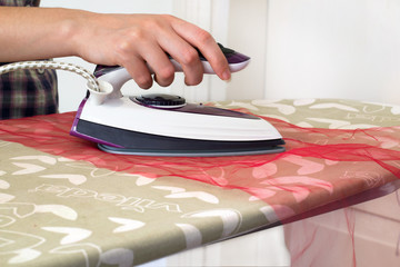 Woman ironing cloth with portable travel iron on ironing board