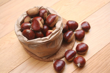 Bunch of ripe chestnuts in a paper bag on wooden background on selective focus