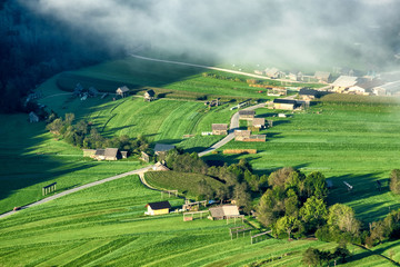 Small farming village in bohinj region of the triglav national park with fog filling up the valley from an aerial perspective