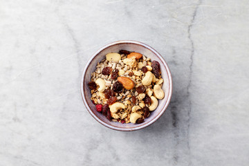 Bowl of granola with nuts, raisins, cranberries and chia seeds. Concept for a tasty and healthy meal. Stone background. Top view. Copy space.