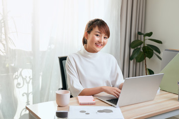 Young Asian beautiful woman works for a computer from a home with a laptop at desk as a freelancer