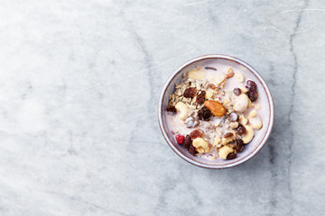 Bowl of granola with yogurt, nuts, raisins, cranberries and chia seeds. Concept for a tasty and healthy meal. Stone background. Top view. Copy space.