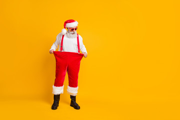 Fototapeta na wymiar Look i lose weight. Full size photo of crazy shocked funny santa claus in red hat show christmas x-mas time dieting effect hold his big size trousers isolated bright color background