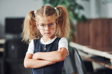 Portrait of offended little girl that stands indoors with her arms crossed