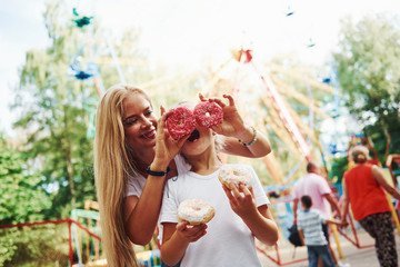 Having fun with donuts. Cheerful little girl her mother have a good time in the park together near attractions