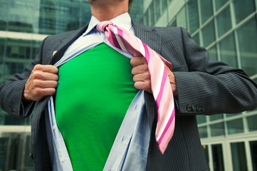 Business superhero ripping off his suit to reveal his green eco-warrior outfit in the courtyard of a modern office complex