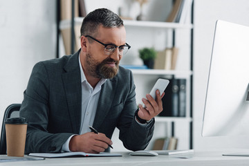 handsome businessman in formal wear holding smartphone and pen