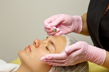 The concept of cosmetology. Close-up of a beautician applying a green mask with a brush on a...