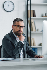 Naklejka premium handsome businessman in formal wear and glasses looking at camera in office