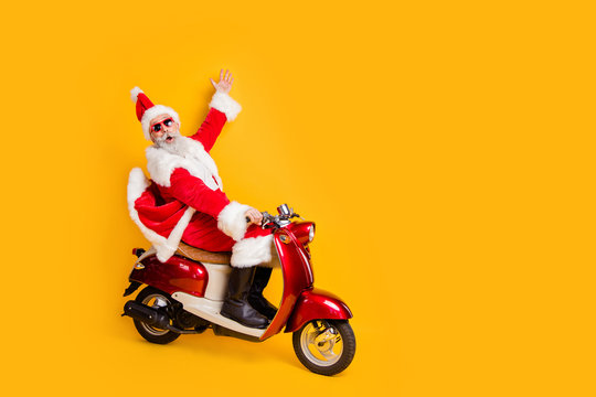 Full body photo of white haired santa riding by bike showing empty space shocking sale x-mas prices wear stylish sun specs red coat pants cap shirt boots isolated yellow color background