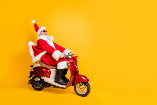 Full body photo of santa white hair grandpa riding speed x-mas party by bike afraid to be late wear trendy sun specs red coat trousers cap shirt boots isolated yellow color background