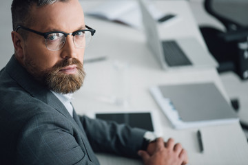 handsome businessman in formal wear and glasses looking at camera in office