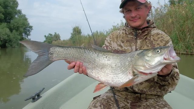 Fishing for Asp. Young angler holds the trophy Asp fish (Leuciscus aspius) and looks into the camera being in the boat on the river