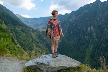 Young female traveler dressed in a poncho stand in the beautiful mountains 