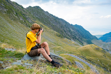 Naklejka na ściany i meble Young male traveler with photocamera in the mountains