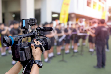 hand holding a video camera with marching band blurred background